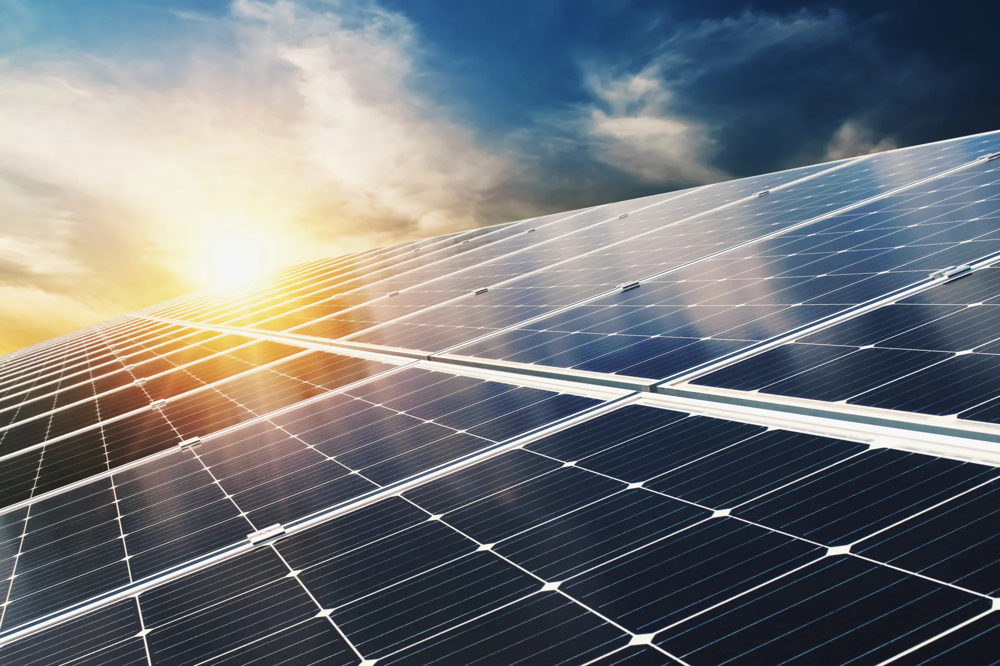 Photovoltaikmodule auf einem Hausdach. Im Hintergrund geht die Sonne unter.